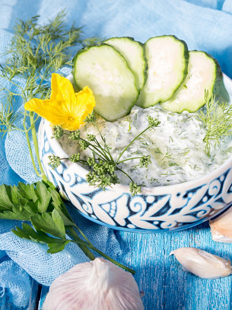 Schälchen mit Zaziki, Gurke,Knoblauch auf blauem Holz