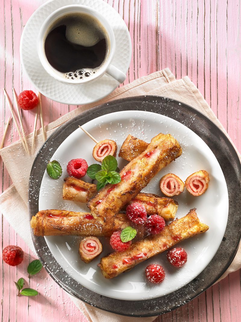 French Toast gerollt auf Teller mit Himbeeren und einer Tasse Kaffee