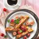 French Toast gerollt auf Teller mit Himbeeren und einer Tasse Kaffee