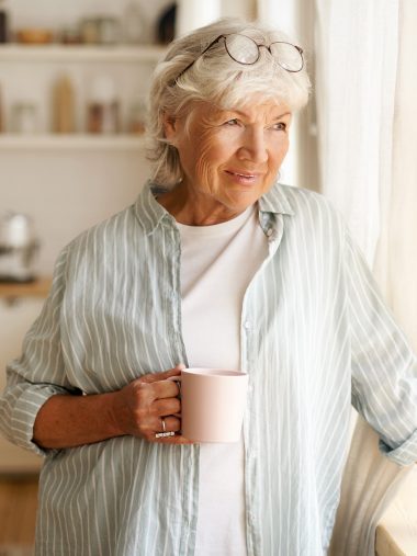 Frau mit Kaffeetasse schaut aus dem Fenster