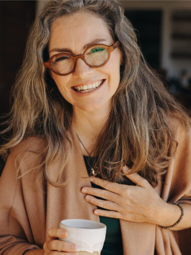 Lächelnde Frau mit Kaffee und Hand auf dem Herzen
