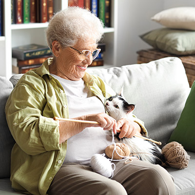 Frau strickt auf dem Sofa und schmust dabei mit ihrer Katze