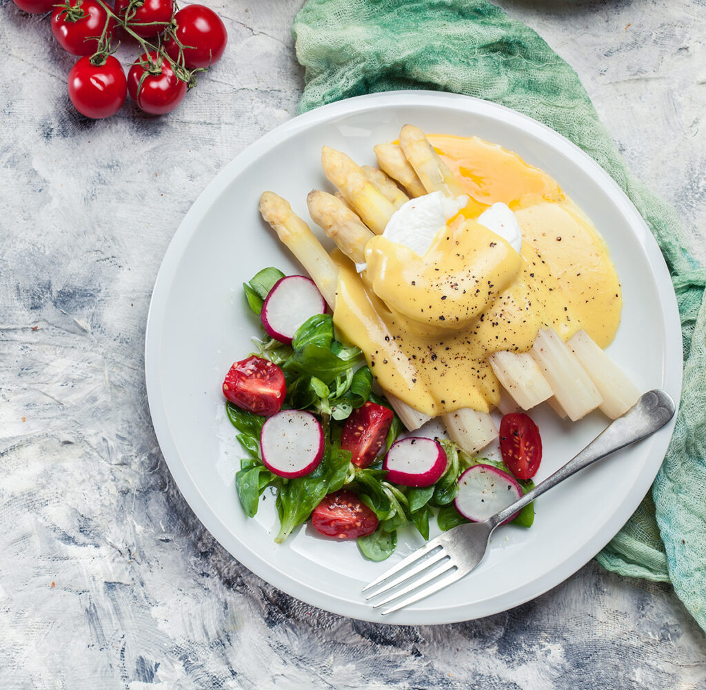 Spargel-Gericht mit pochiertem Ei, Sauce Hollandaise und Feldsalat mit Radieschen und Cocktailtomaten auf einem Teller