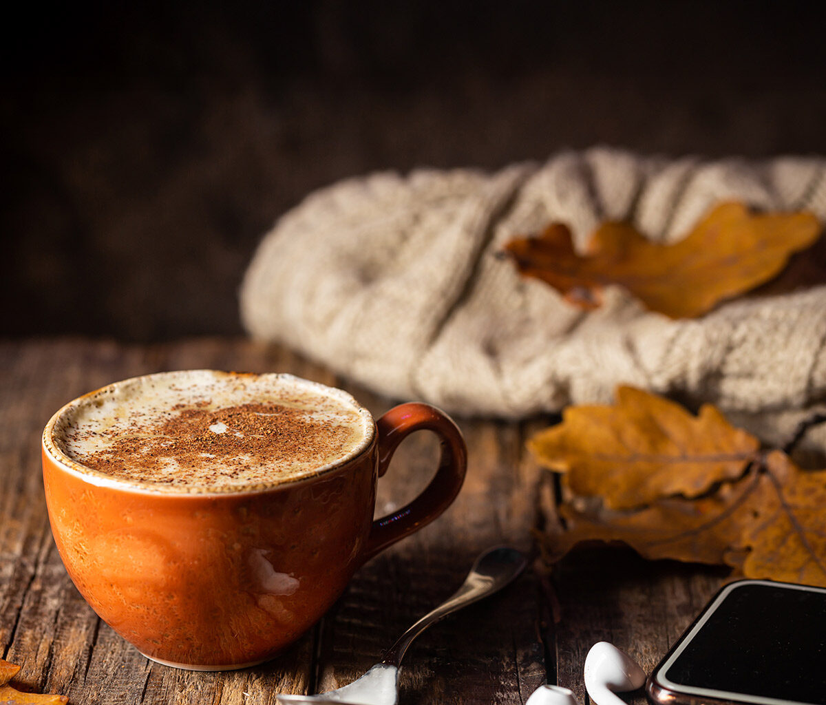 Kaffee und Kopfhörer liegen in einem herbstlich-rustikalen Ambiente