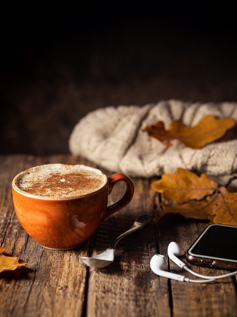 Kaffee und Kopfhörer liegen in einem herbstlich-rustikalen Ambiente