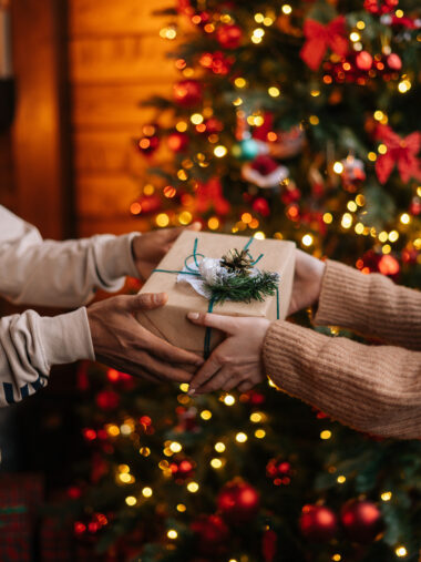 Weihnachtsgeschenk übergeben vorm Weihnachtsbaum