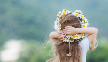 Kind mit geflochtener Gänseblümchen-Krone im weißen Blumenfeld