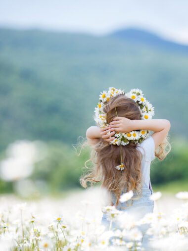 Kind mit geflochtener Gänseblümchen-Krone im weißen Blumenfeld