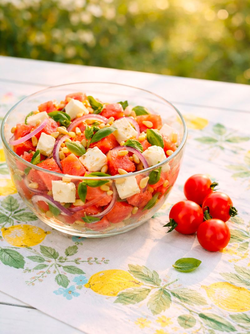 Melonen-Feta-Salat in einer Schüssel, daneben Tomaten