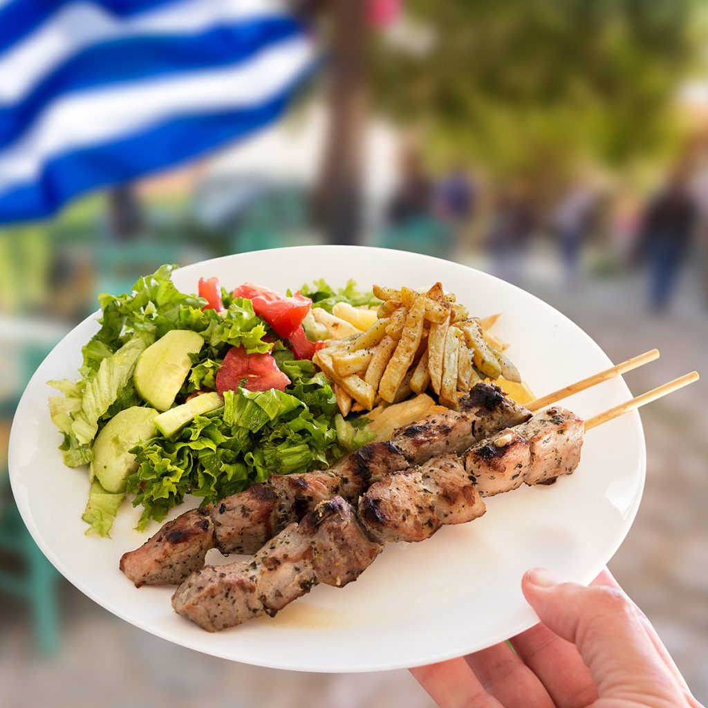 Souvlaki auf Teller angerichtet, im Hintergrund eine griechische Flagge