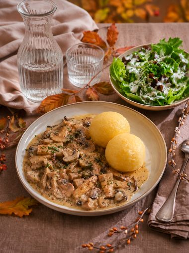 Teller mit Pilzgulasch und Klößen angerichtet auf einem herbstlichen Tisch