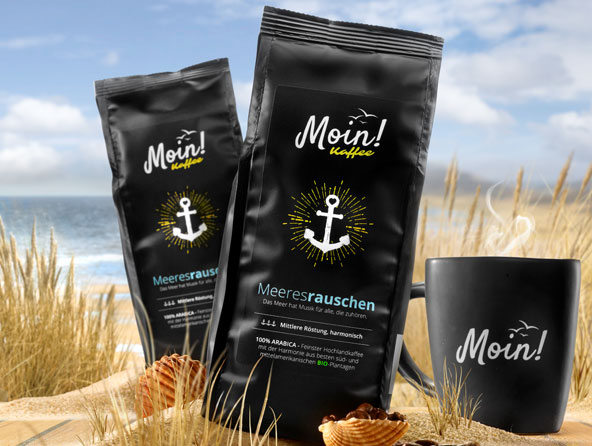 Moin Kaffee-Packungen und Tasse in Dünen mit Meer im Hintergrund