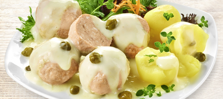 Königsberger Klopse mit Kapernsauce, Kartoffeln und Salat auf weißem Teller.