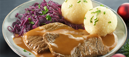 Festtagsgericht mit Rinderbraten, Rotkohl und Klößen auf Teller