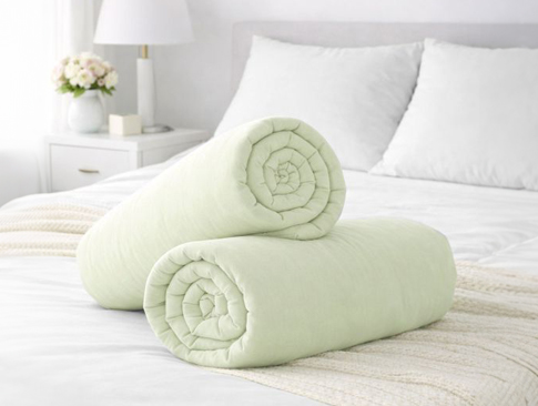 Grüne Spannbettlaken aus Baumwolle auf weißem Bett dekorativ gerollt