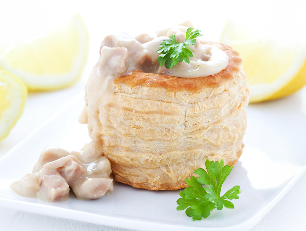 Blätterteigpastete mit Ragout-Füllung, dekoriert mit Petersilie und Zitrone