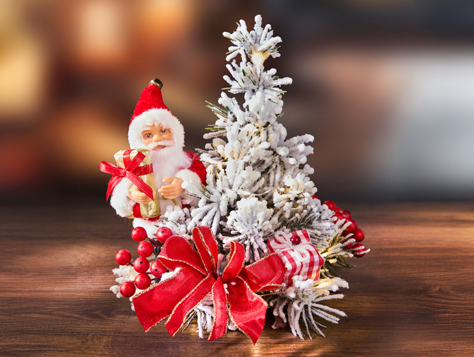 Weihnachtsdekoration mit Santa-Figur, Schneetanne, roten Schleifen und festlichen Beeren auf Holztisch