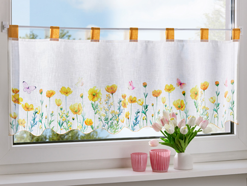 Kurzgardine mit gelbem Blumenmuster an einem Fenster mit Deko.