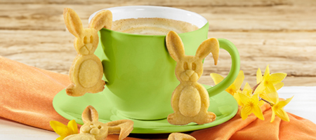 Süße Hasen-Tassenkekse an einer grünen Kaffeetasse mit Osterdeko und Blumen.