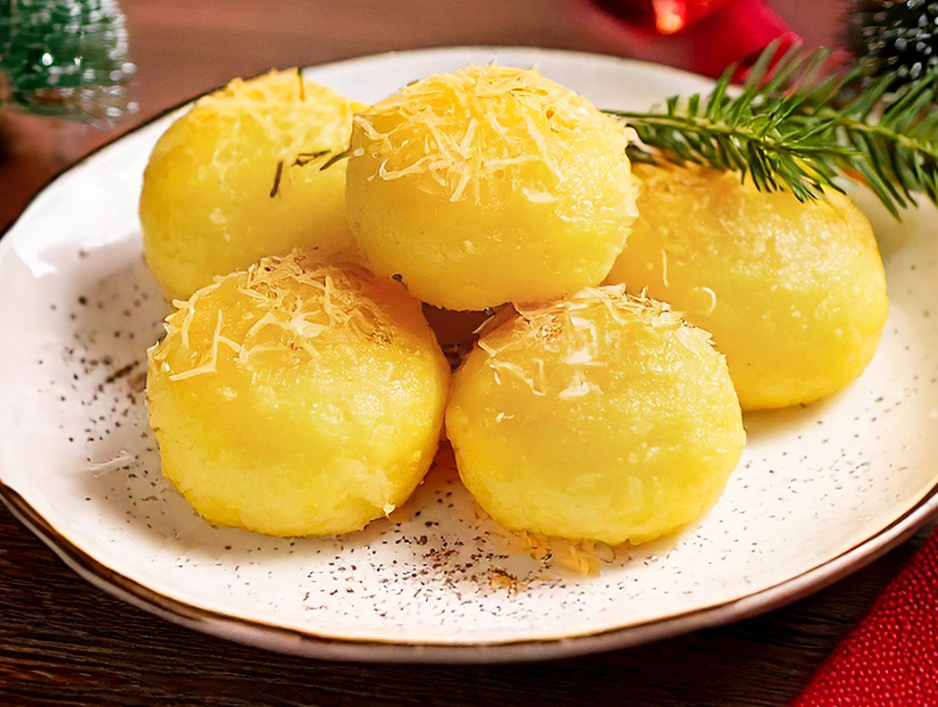 Fünf Reibeknödel mit geriebenem Käse, angerichtet auf einem weißen Teller
