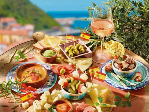 Spanische Tapas mit Oliven, Käse, Chorizo und Wein vor mediterraner Kulisse