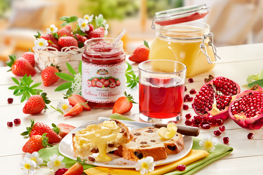 Frühstück mit Erdbeermarmelade, Saft, Granatapfel und Hefezopf auf gedecktem Tisch