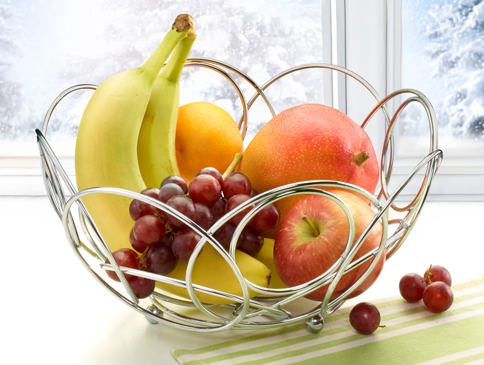 Metall-Obstkorb mit Banane, Apfel, Trauben und Orange am Fenster