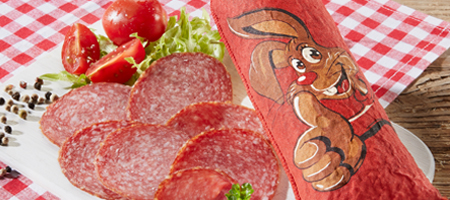 Ostersalami mit Hasenmotiv, serviert mit Tomaten und Salat auf rustikalem Tisch.