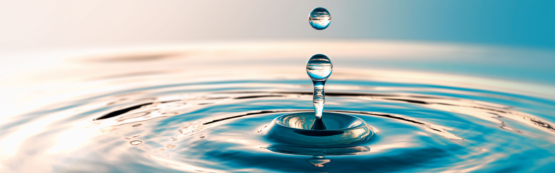 Wassertropfen erzeugt konzentrische Wellen auf ruhiger Oberfläche