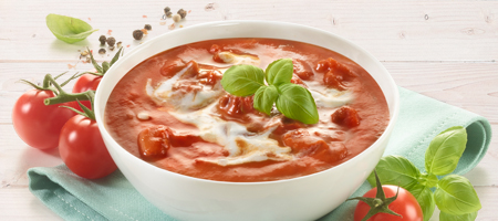 Tomatensuppe mit Sahne und Basilikum in weißer Schale serviert