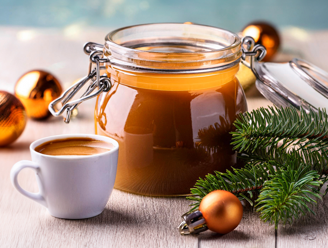 Karamellsauce im Glas mit einer Tasse Kaffee, dekoriert mit Weihnachtskugeln