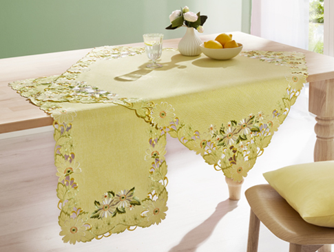 Gelbe Tischdecke mit besticktem Blumenmuster auf Holztisch.