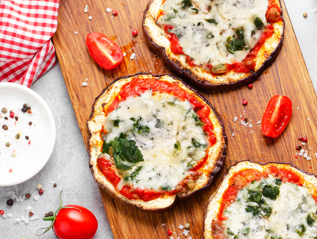 Auberginen-Pizza mit Spinat dekoriert auf einem Holzbrett mit kleinen Cherry-Tomaten