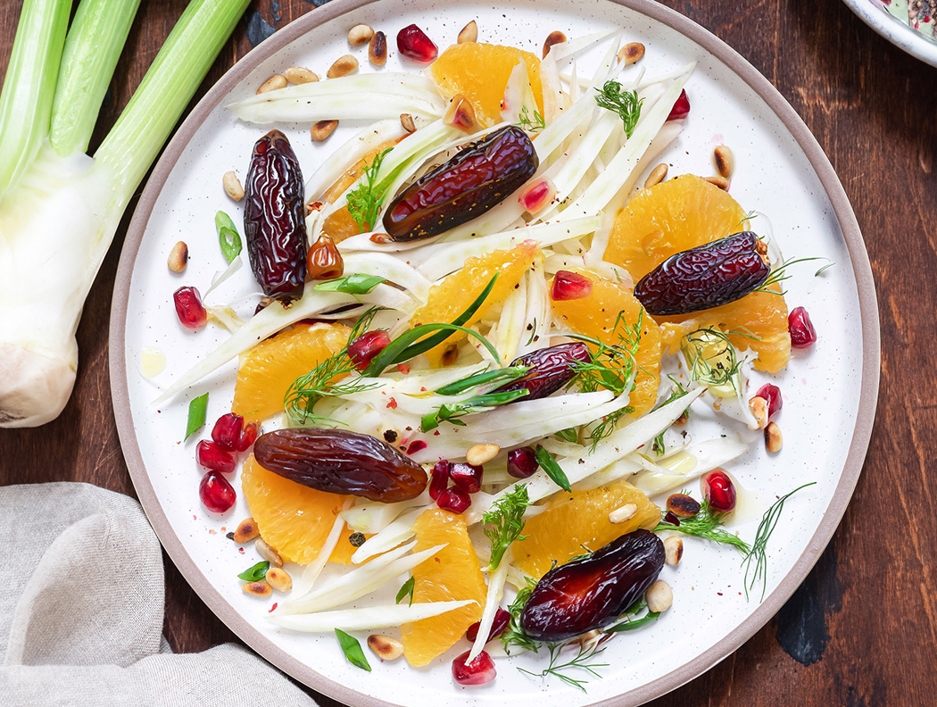Fenchel-Orangen-Salat mit Datteln, Granatapfelkernen und Pinienkernen auf Teller